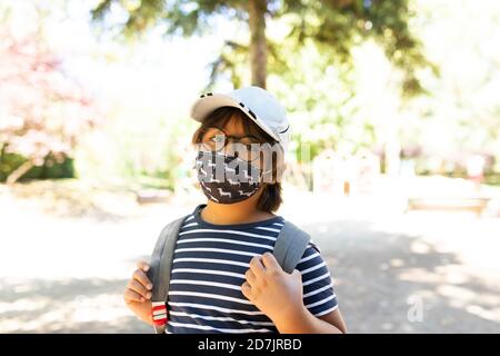 Schoolboy wearing mask standing on footpath Stock Photo