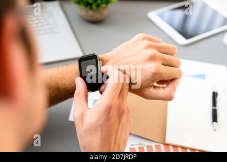 Man looking at smart watch while sitting by desk at office Stock Photo