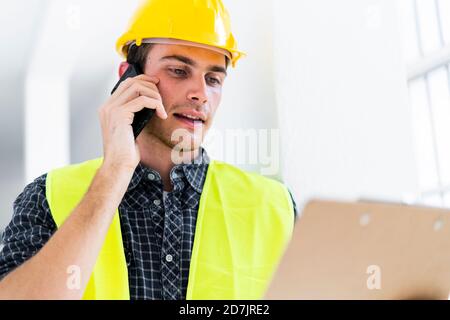 Architect holding notepad while talking on mobile phone at construction site Stock Photo