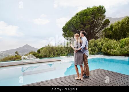 Heterosexual couple looking at view with wine glass standing near pool Stock Photo