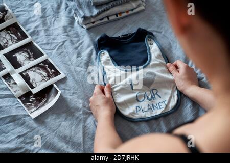 Pregnant woman folding baby clothes by ultrasound on bed at home