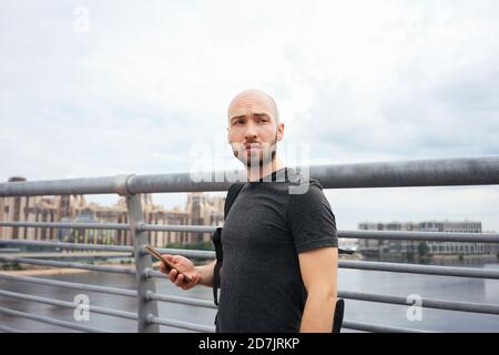 Young man using smart phone looking away while standing by railing against sky Stock Photo