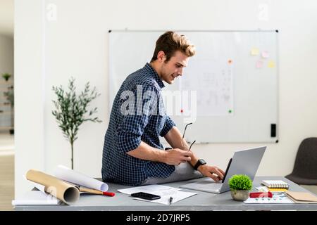 Young man using laptop while sitting on desk at office Stock Photo