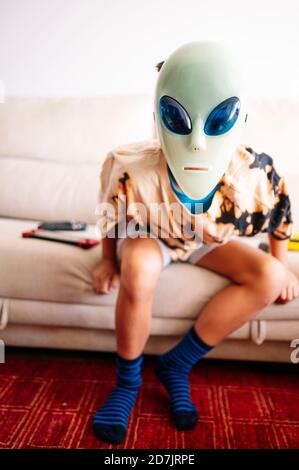 Boy wearing alien mask sitting on sofa at home Stock Photo