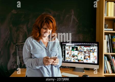 Mature woman using phone while standing by desk at home Stock Photo