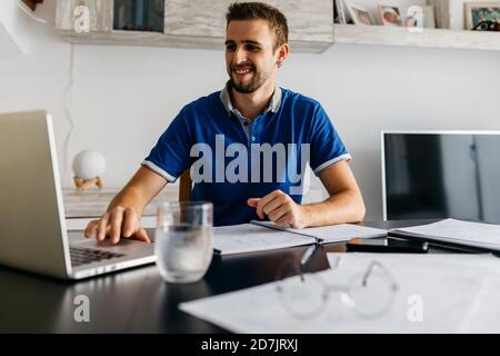 Smiling handsome young man using laptop while doing homework at table Stock Photo