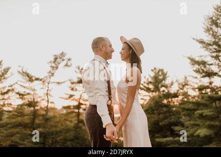 Bride and bridegroom looking at each other while standing in forest during sunset Stock Photo