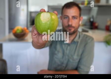 Man showing bitten apple while sitting at home Stock Photo