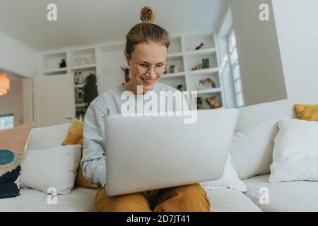 Smiling woman working on laptop while sitting on sofa at home Stock Photo
