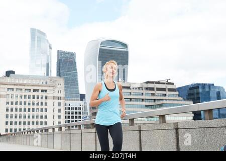 Mature blond woman running on footbridge against modern office buildings at downtown in city Stock Photo