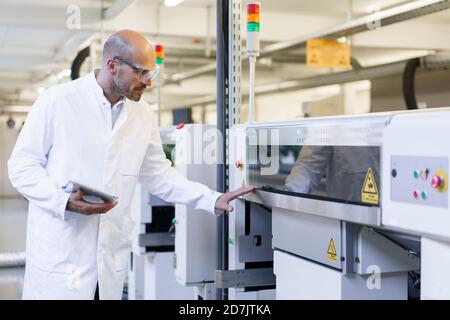 Mature male technician holding digital tablet examining machinery at factory Stock Photo