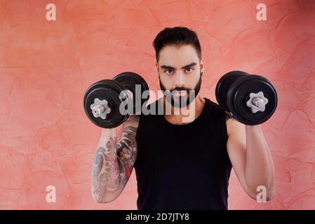 Mid adult man lifting dumbbell while standing against brown wall Stock Photo