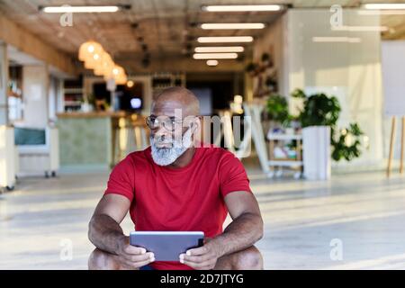 Thoughtful man holding digital tablet and looking away while sitting at rooftop Stock Photo