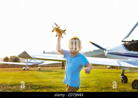 Cute little boy playing with toy plane while standing at airfield Stock Photo