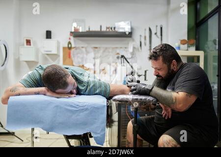 Male artist tattooing on customer's hand in studio Stock Photo