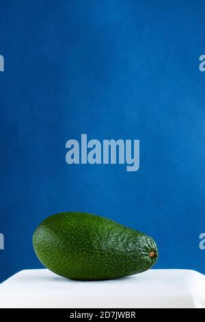 green fresh avocado on a white table against blue background, minimalistic  picture  with space for text Stock Photo