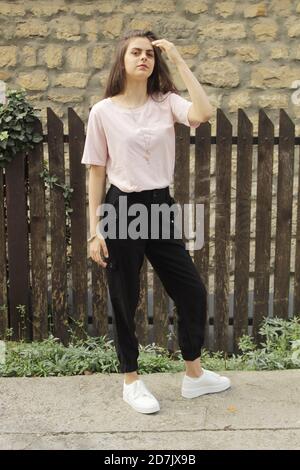 Young girl poses in front of a stone wall and a wooden fence Stock Photo