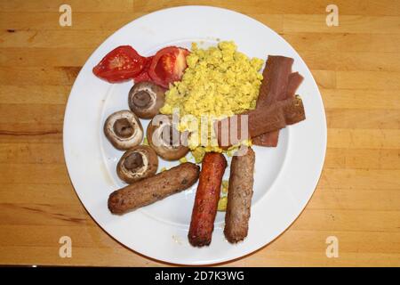 Close up vegan breakfast dairy meat free delicious full English vegetarian tofu spice scramble mock egg, plant bacon sausages tomatoes mushroom, beans Stock Photo