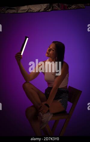 Woman holds LED lamp looking on it against of purple background. Presentation of Nanlite Studio Lighting. Backstage concept. June 2020, Kiev Ukraine Stock Photo