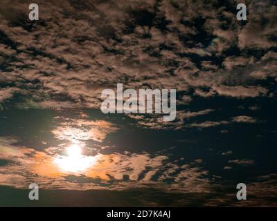 Evening orange sunny sunset behind white clouds on blue sky. Stock Photo