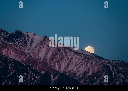 full moon hiding behind the andes mountain range in mendoza argentina Stock Photo