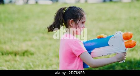 Girl playing with a water gun in the garden wearing a pink t-shirt Stock Photo
