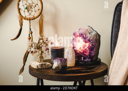 Relaxing home shrine with relaxing objects, amethyst cluster geode lamp illuminated, scented candle burning, selenite tower stone, crystal wire tree. Stock Photo