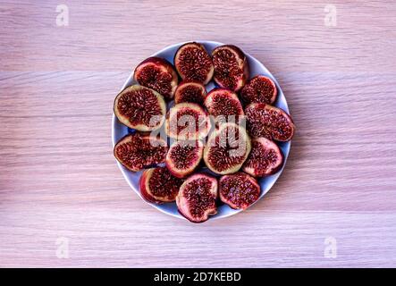 Ripe figs cut into halves in a plate on a light wooden background close-up. View from above Stock Photo
