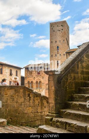Tourist women with hats on the stairs of the Duomo of San Gimignano admiring the main square with the medieval Torre Chigi, Siena, Tuscany, Italy Stock Photo