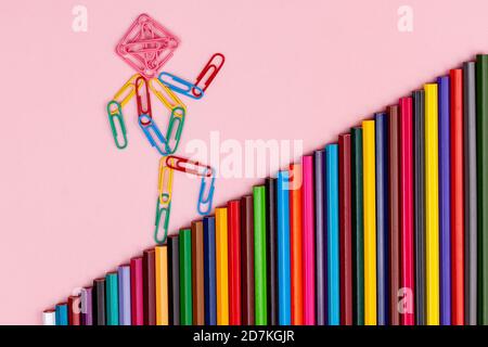 man from multi-colored paper clips goes up the stairs from multi-colored pencils isolated Stock Photo