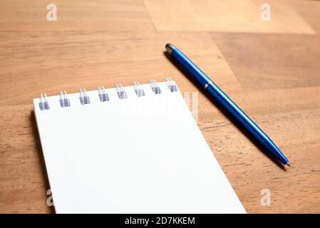 Spiral notebook, opened on a blank page, next to a blue pen, on a wooden desk. Close subjective view. Stock Photo