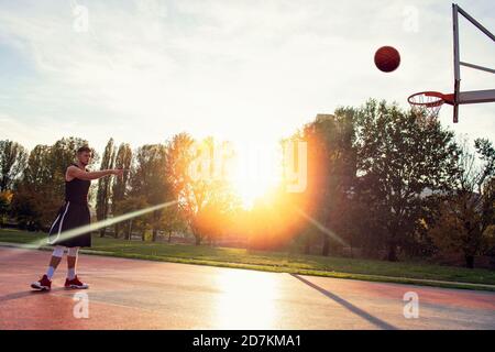 Young man jumping and making a fantastic slam dunk playing streetball, basketball. Urban authentic. Stock Photo