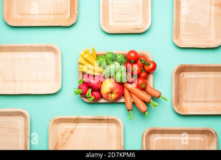 Top view with fresh vegetables in a zero-waste tray. Eco-friendly palm leaf plates on a green-colored background. Stock Photo