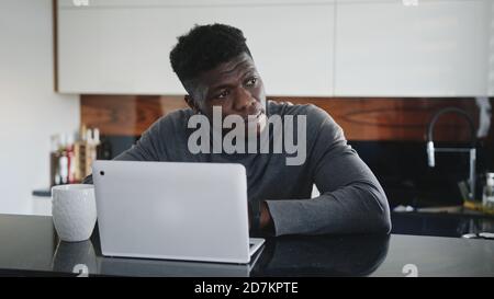 young african american black man working on laptop in his appartment stretching and looking through the window. High quality photo Stock Photo