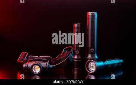 Head and pocket flashlights on a dark background. Modern lanterns illuminated with red-blue light. Stock Photo