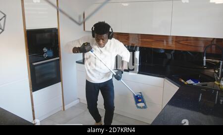 Happy handsome black man listening to the music and using broom as guitar. tidying up appartment. High quality photo Stock Photo