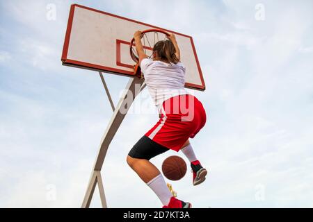 Females playing basketball on street court. Woman streetball player making slam dunk in a basketball game. Stock Photo