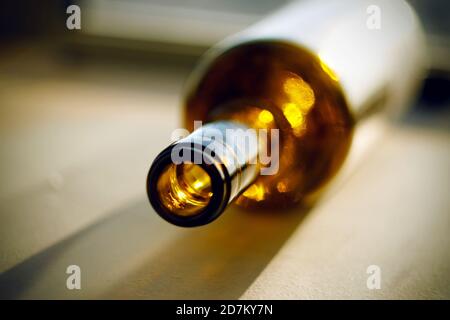 An empty bottle of strong alcohol, left after drinking, lies on the sunlit surface and shimmers Stock Photo