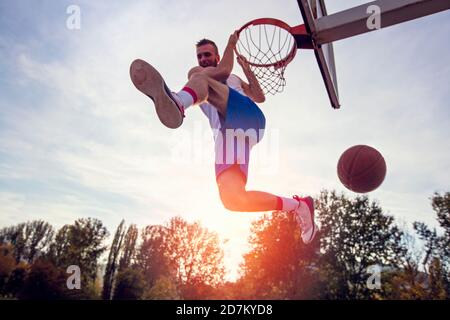 Young man jumping and making a fantastic slam dunk playing streetball, basketball. Urban authentic. Stock Photo