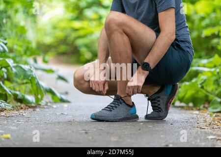 Running fit man tying shoes wearing wearable technology smart watch. Fitness runner athlete getting ready to train for marathon start in spring autumn Stock Photo