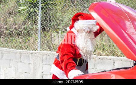 Santa Claus worried looking at the engine of his damaged car at Christmas on a street outside Stock Photo