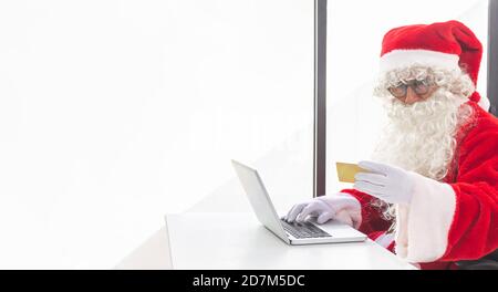 Santa Claus working on a laptop in a minimalist white office at Christmas. Text space Stock Photo