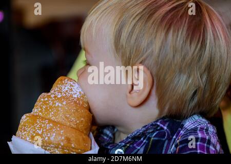 Close up hand little boy having breakfast in cafe in beautiful kid eating croissant bun chocolate the table in restaurant eco paper bag. Stock Photo