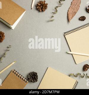 Notebooks with dry leaves, pine cones on gray background. flat lay, top view, copy space. Work and study place. Autumn and winter concept Stock Photo