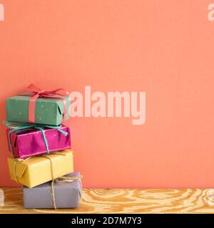 Stack of colorful gift boxes on wooden table with coral pink background Stock Photo