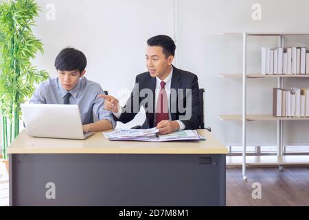 An Asian male supervisor teaches the newcomer to the office on his desk. Stock Photo