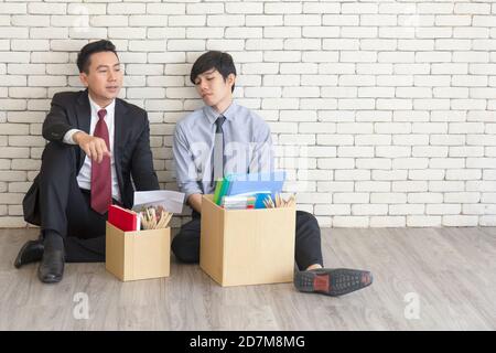 Two male employees sat on the floor talking in front of each other with a cardboard box for personal use after being fired from work. Stock Photo