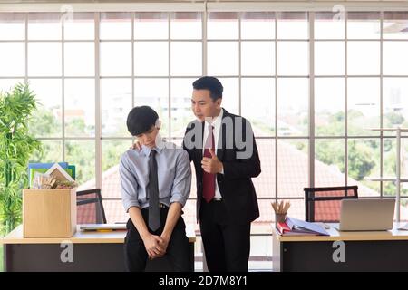The supervisor stands to encourage an Asian male subordinate beside a desk in the office. Stock Photo