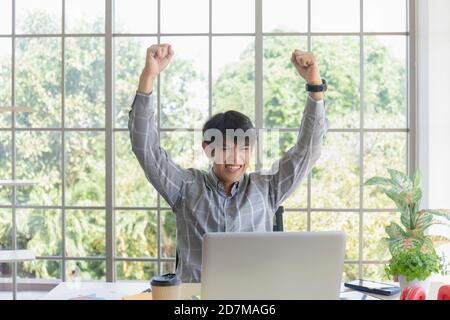 A young businessman in Asia showed his joy on a desk beside a glass window balcony. Stock Photo