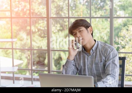 A young Asian businessman talking on the phone on a balcony window desk. Stock Photo